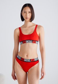 Ensemble de bikini rouge comprenant un haut de style débardeur et des culottes taille basse. Les deux pièces sont ornées d'un bandeau élastique noir avec le logo "DIESEL".