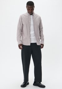 Camisă cu mânecă lungă de culoare gri deschis, textur�ă din bumbac, purtată peste un tricou alb, asortată cu pantaloni largi negri și pantofi negri strălucitori.