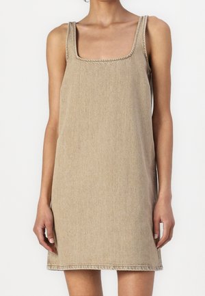 Robe en denim beige sans manches avec un col carré portée par une femme, visible des épaules jusqu'au milieu des cuisses sur un fond uni.