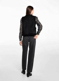 Svart ärmlös väst med pälsbesättning, lager ovanpå en långärmad blommig blus. Modell bär mörkgrå raka jeans och svarta stövlar.