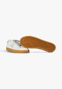 Zapatillas blancas con una parte superior de cuero liso, cordones con patrón y una suela de goma texturizada con un patrón de espiga.