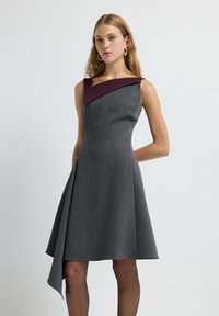 Graues ärmelloses Kleid mit asymmetrischem burgunderfarbenem Ausschnitt und volantartigem Rock. Hergestellt aus strukturiertem Stoff, mit seitlichem Drapierungselement.
