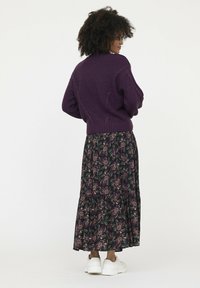 Pull en tricot violet avec un détail en torsade, associé à une jupe à motifs floraux dans des teintes sombres, et des baskets blanches.