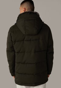 Donkergroene donsjas met horizontale naden, een met bont gevoerde capuchon en elastische manchetten. Het materiaal lijkt glad en geïsoleerd.