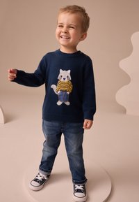 Suéter azul marino con diseño de mapache, que lleva una camiseta amarilla a rayas, combinado con jeans azules y zapatillas negras. Botones decorativos en el hombro.