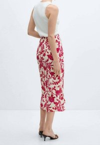 Gonna midi floreale color crema con motivi rosa. Design aderente, tessuto strutturato e orlo leggermente svasato. Abbinata a un top bianco e sandali.