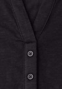 Close-up of black knitted cardigan with V-neck and two visible black buttons fastened down the front.