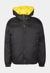 Svart puffjacka med en ljusgul innerfoder, dragkedja framtill och elastiska ärmslut. Har en huva för extra värme och komfort.