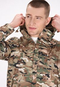 Camo-jas in een mix van groen, bruin en beige kleuren. Het heeft een hoge kraag, een verstelbare capuchon en ritszakken.