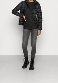 Svart puffjacka med huva, grå stickad långärmad tröja, grå smala jeans och svarta snörade stövlar. Grön axelremsväska ingår.