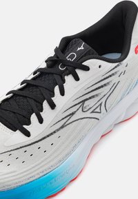 Scarpa da corsa con tomaia bianca e mesh nero e lacci. Accenti notevoli di sole blu e rosso, e linee di design eleganti in nero e grigio.