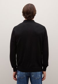 Maglione nero lavorato a maglia con collo rotondo, maniche lunghe e polsini a costine, abbinato a jeans in denim azzurro chiaro. Visuale posteriore visibile.