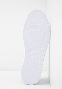 Biała podeszwa obuwia z teksturowaną powierzchnią, na której znajdują się okrągłe wzory i wypukłe kropki, z logo na środku.
