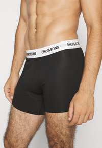 Schwarze Baumwollboxershorts mit einem weißen elastischen Bund, der den Text "ONLY & SONS" trägt. Das Design ist eng anliegend mit sichtbaren Nähten.