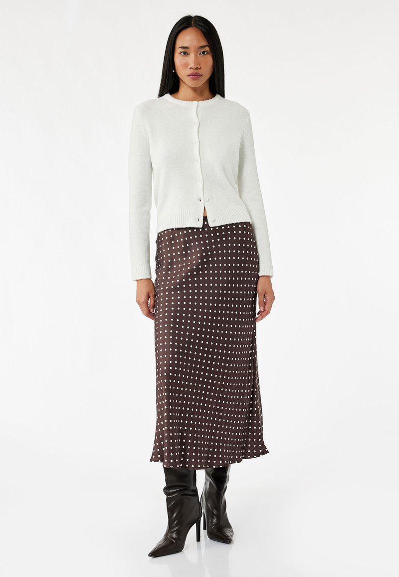 Vit stickad cardigan med knappar, kombinerad med en brun prickig satinmidikjol och svarta knähöga klackstövlar. Slät textur.