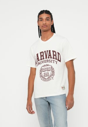 Weißes Baumwoll-T-Shirt mit "HARVARD UNIVERSITY" in Burgunderrot. Mit einem Wappen, auf dem "VERITAS" steht, und einem kleinen Etikett am Saum.