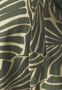 Tessuto decorato con motivi ispirati alle foglie in verde e beige. Il materiale sembra tessuto con una finitura testurizzata, che mette in risalto linee audaci e fluide.