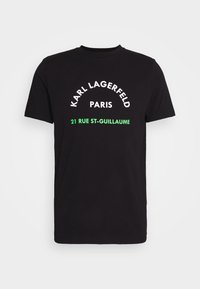 černé bavlněné tričko s bílým a zeleným nápisem, včetně "KARL LAGERFELD," "PAŘÍŽ" a "21 RUE ST-GUILLAUME," v klasickém designu.