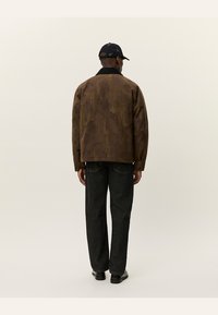 Braune strukturierte Jacke mit schwarzem Kragen, kombiniert mit dunklen Jeans. Die Jacke hat eine lässige Passform und dezente Designdetails.
