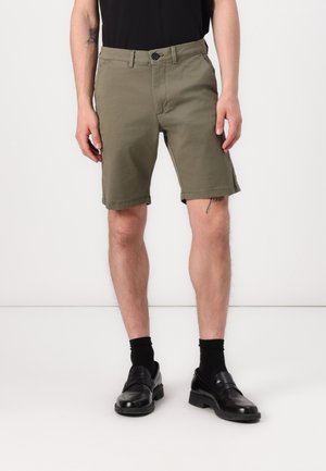 Shorts en khaki avec une coupe droite, dotés d'une fermeture à bouton, d'un ourlet roulé et d'une texture de tissu subtile. Portés avec des mocassins noirs et des chaussettes.
