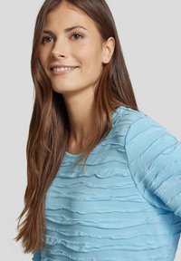 Helles blaues strukturiertes Sweatshirt mit einem welligen, schichtartigen Design, weichem Stoff, runder Ausschnit und langen Ärmeln.