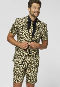 Geltonos, juodos ir oranžinės leopardų rašto kostiumas, su trumpomis rankovėmis ir šortais, derinamas su juoda marška ir kaklaskariu.