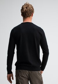 Schwarzer Strickpullover mit langen Ärmeln und rundem Ausschnitt. Weiche Textur, figurbetonte Silhouette, gerippter Saum und Bündchen. Keine sichtbaren Muster.