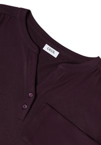 Paarse T-shirt met korte mouwen en een V-hals, voorzien van twee knopen en een borstzak. Zachte stof met een gladde textuur en een relaxte pasvorm.