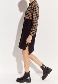 Sukienka w kratkę z czarną spódnicą, z kołnierzykiem, długimi rękawami, bocznymi rozcięciami, w zestawie z czarnymi, masywnymi botkami za kostkę.