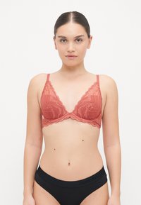 Mežģīņu bralette pelēkā korāļa tonī ar viļņotām malām un regulējamiem siksniņām, apvienots ar melniem augstas jostas biksēm ar logo detaļām.