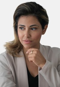 Ritratto di una donna con capelli castano medio e riflessi biondi, che indossa un blazer beige chiaro sopra una maglietta nera, tenendo il mento tra le mani.