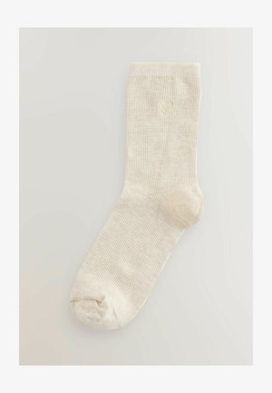 Beige geribde sok met een textuurafwerking. Voorzien van een klein hartjeslogo op het enkelgebied. Standaard crewlengte met een ronde teen.