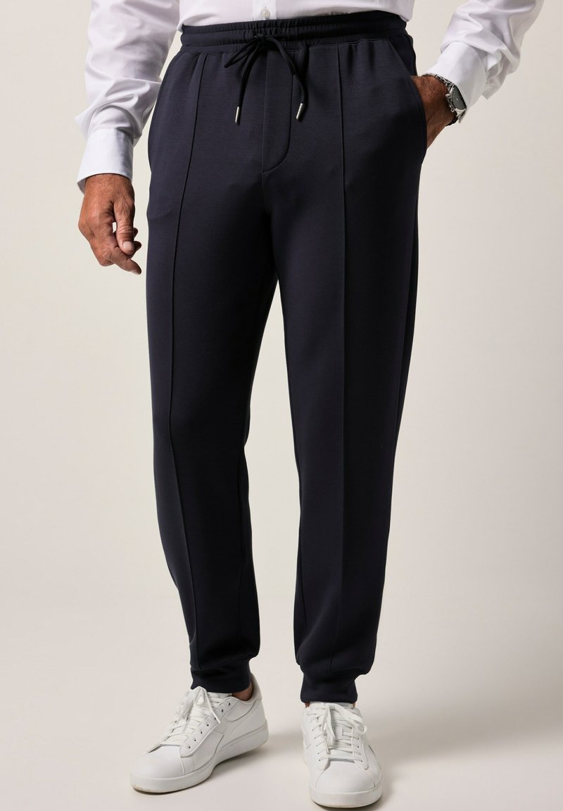 Granatowe spodnie dresowe wykonane z miękkiego materiału, z paskiem na sznurku w talii, bocznymi kieszeniami oraz kontrastowymi detalami szwów. W zestawie z białymi trampkami.