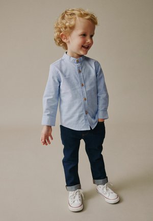 Light blue button-up shirt with a band collar, dark blue jeans, and white sneakers. The shirt features wooden buttons and rolled-up sleeves.