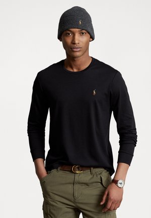 Zwart longsleeve shirt met een klein logo, gecombineerd met olijfgroene cargobroek, een bruine riem en een grijze gebreide beanie. Opmerkelijke horloge om de pols.