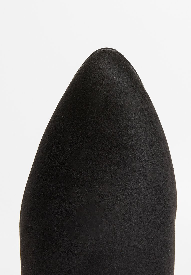 Chaussure en daim noir à bout pointu avec une texture lisse et une silhouette épurée, dotée d'un talon haut et d'un design minimaliste.