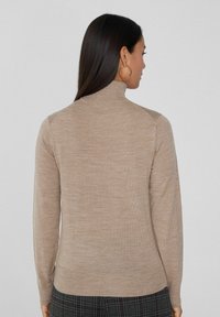Suéter beige de cuello alto hecho de una tela suave y texturizada. Presenta mangas largas y un diseño ajustado, con un dobladillo acanalado.