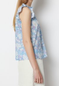 Blaues blumiges ärmelloses Oberteil mit Rüschenausschnitt; zeigt weiße und rosa Blumen; leichtes Material; lockere Passform.