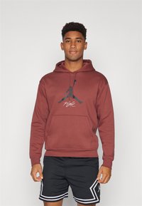 Felpa bordeaux con tasca frontale e logo Jumpman nero. Abbinata a pantaloni corti neri con accenti bianchi e texture perforata.