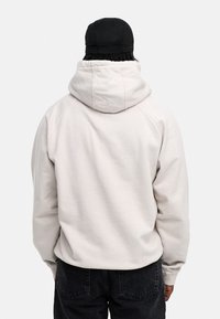 Hellgrauer Kapuzenpullover mit lässiger Passform, sichtbaren Nähten und weichem Material, kombiniert mit schwarzen Hosen.