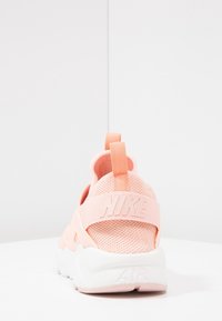 Nike tenisky, pohled zezadu, s růžovým síťovaným svrškem, bílou gumovou podrážkou a logem na pásku. Ozdobené poutkem pro snadné obutí.