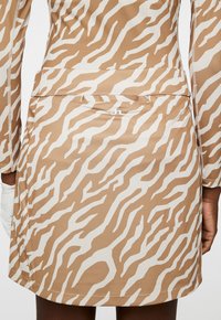 Brun och grädde mönstrad klänning med zebramönster, tillverkad av ett mjukt tyg, med en bakficka och en logotyp på midjebandet.