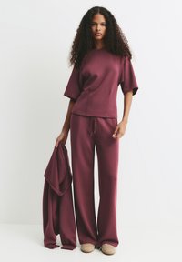 Burgundský lounge set vyrobený z měkké látky; volně střižený top s krátkými rukávy, kalhoty se šňůrkou, udržované s dalším odpovídajícím vrstvou.