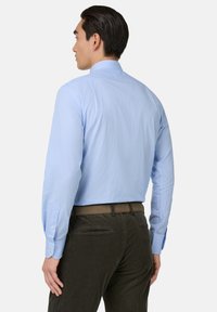 Lichtblauwe, langemouwen overhemden met een geblokt patroon. Beschikt over knoopmanchetten en een ontwerp op de achterkant van de kraag. Gepaard met donkere corduroy broeken.