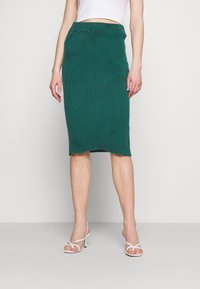 Zelená vypasovaná midi sukně z žebrovaného úpletu s úzkým pasem a jemným lemem. Materiál má měkkou texturu, která podtrhuje její přiléhavý design.