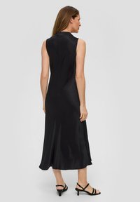 Czarna sukienka bez rękawów o gładkiej, satynowej strukturze, w kształcie litery A, osiągająca długość do kolan, z wysokim dekoltem. W połączeniu z czarnymi sandałami na szpilkach.