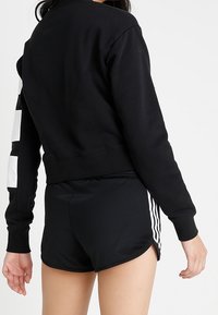 Black sweatshirt with a cropped design and white logo detail on the left sleeve, paired with black shorts featuring side stripes.