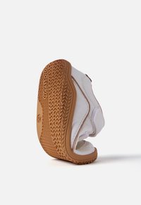 Sándal de playa blanca con parte superior texturizada, suela de goma marrón y costuras visibles. Presenta un diseño de punta abierta y una plantilla acolchada.