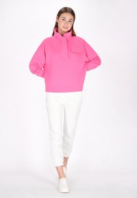 Felpa rosa con cappuccio alto, tasca frontale e orlo a coste, abbinata a pantaloni della tuta bianchi a sigaretta e sneakers bianche.
