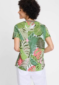 Korte mouwen shirt van lichtgewicht stof met een groene achtergrond en tropische bladranden in verschillende tinten groen, roze en wit.
